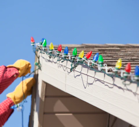 close up shot person installing led christmas lights on house roof